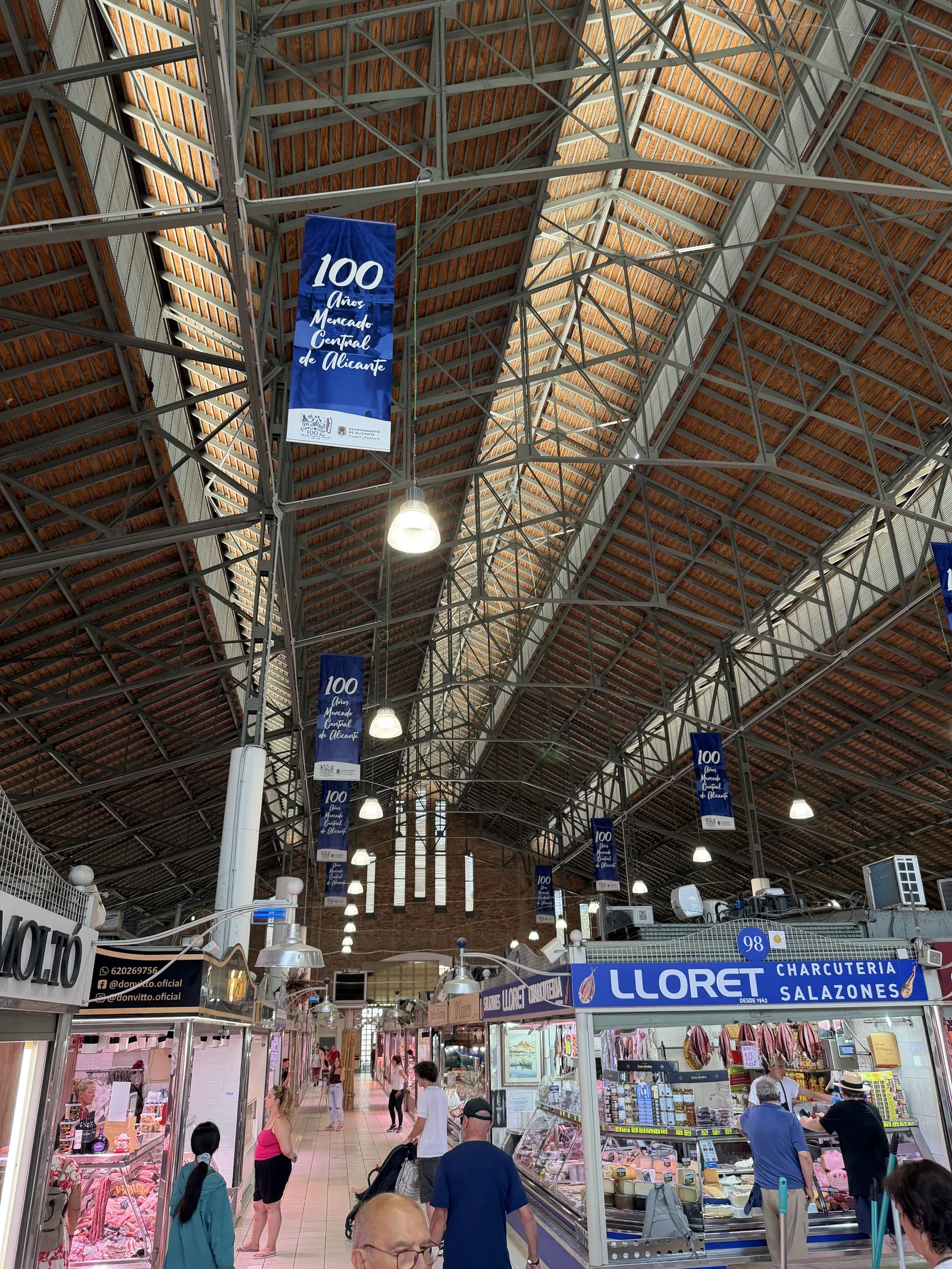 Interior del Mercado Central de Alicante, con su gran estructura de madera y metal y las banderolas del centenario